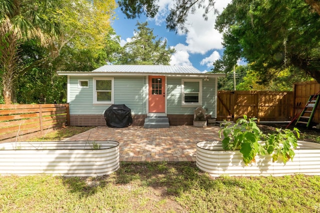 rear view of house with entry steps, a fenced backyard, metal roof, and a patio area