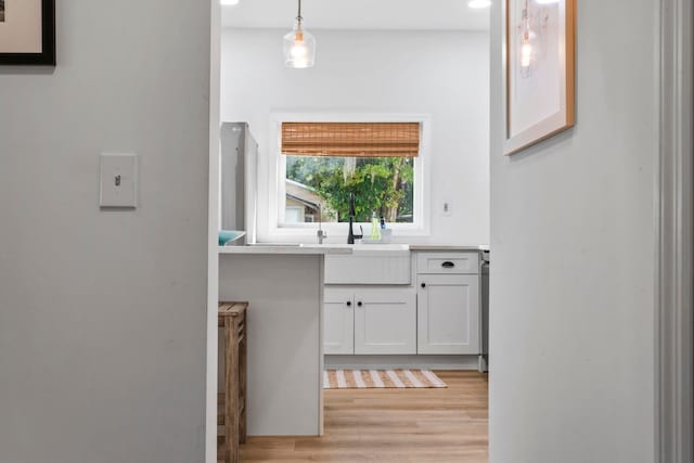 kitchen featuring light countertops, white cabinets, light wood finished floors, a sink, and hanging light fixtures