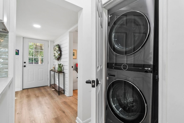 washroom with stacked washing maching and dryer, light wood-type flooring, and laundry area