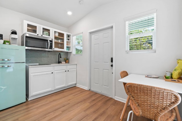kitchen featuring stainless steel microwave, white cabinetry, freestanding refrigerator, lofted ceiling, and a sink