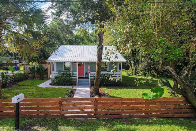 view of front of property featuring a front yard, metal roof, a fenced front yard, and covered porch