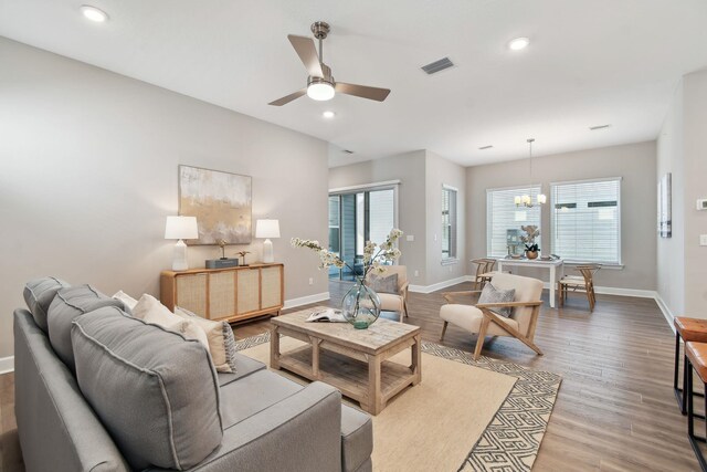 living room featuring wood finished floors, ceiling fan with notable chandelier, visible vents, and baseboards