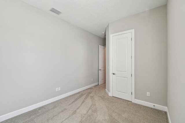 empty room with visible vents, light colored carpet, a textured ceiling, and baseboards