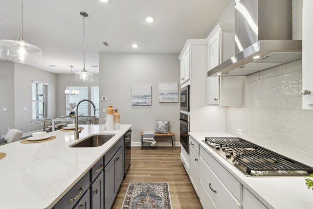 kitchen featuring wood finished floors, a sink, appliances with stainless steel finishes, white cabinetry, and wall chimney range hood
