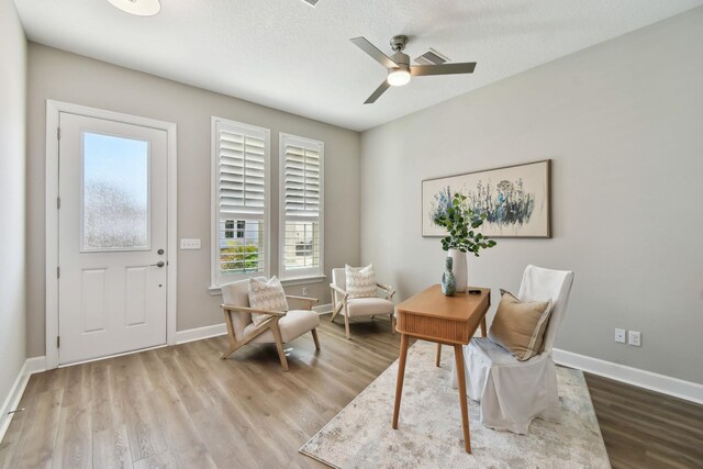 living area featuring a textured ceiling, a ceiling fan, baseboards, and wood finished floors