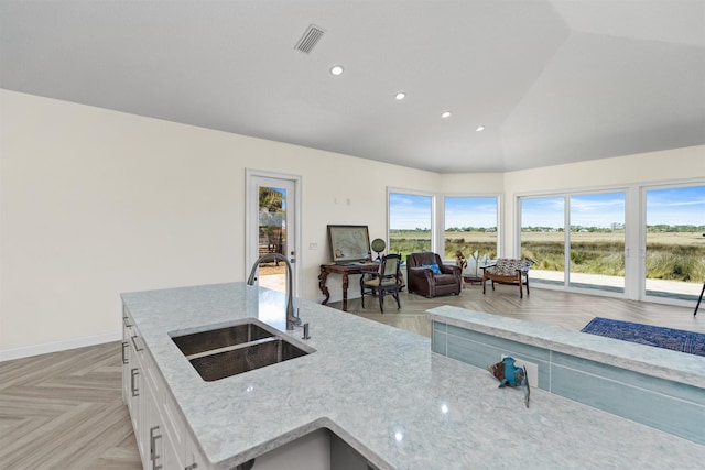 kitchen featuring a sink, visible vents, white cabinets, vaulted ceiling, and light stone countertops