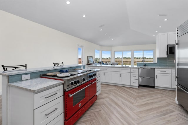 kitchen with white cabinets, premium appliances, light stone counters, a sink, and recessed lighting