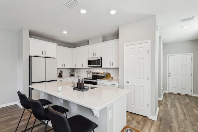 kitchen featuring stainless steel appliances, white cabinetry, a breakfast bar, and an island with sink