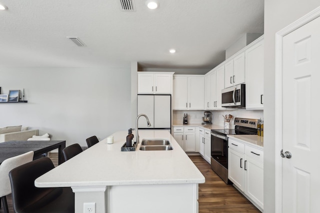 kitchen with a breakfast bar, an island with sink, white cabinets, and appliances with stainless steel finishes