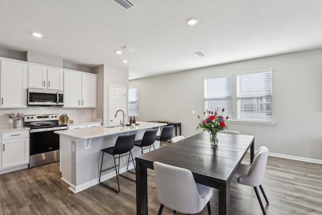 kitchen with sink, tasteful backsplash, a center island with sink, stainless steel appliances, and white cabinets