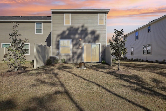 back house at dusk with a yard and central AC