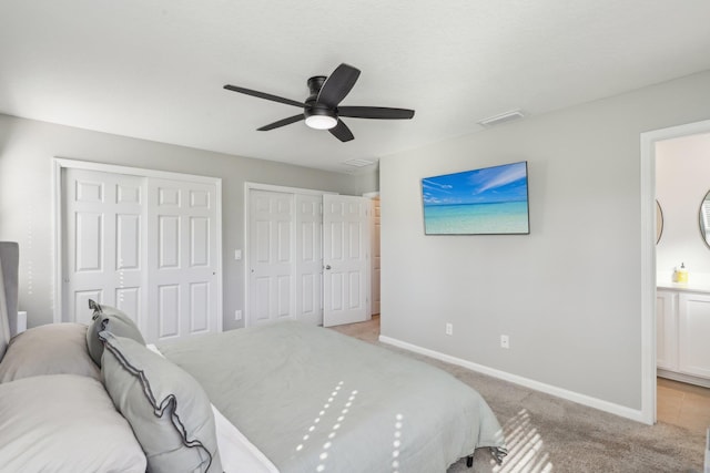 bedroom with ceiling fan, light carpet, two closets, and ensuite bath