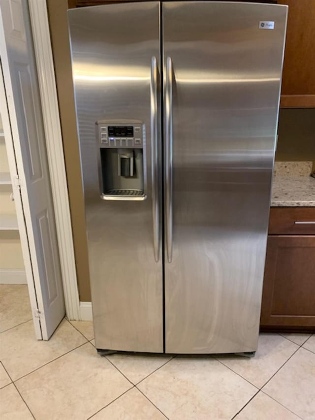 kitchen featuring light stone countertops, light tile patterned floors, and stainless steel refrigerator with ice dispenser