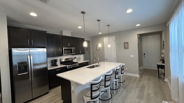 kitchen featuring an island with sink, stainless steel appliances, dark cabinetry, and a sink