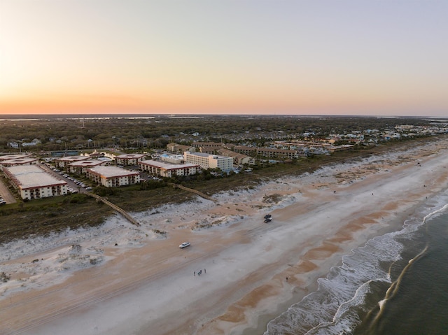 aerial view at dusk featuring a water view and a view of the beach