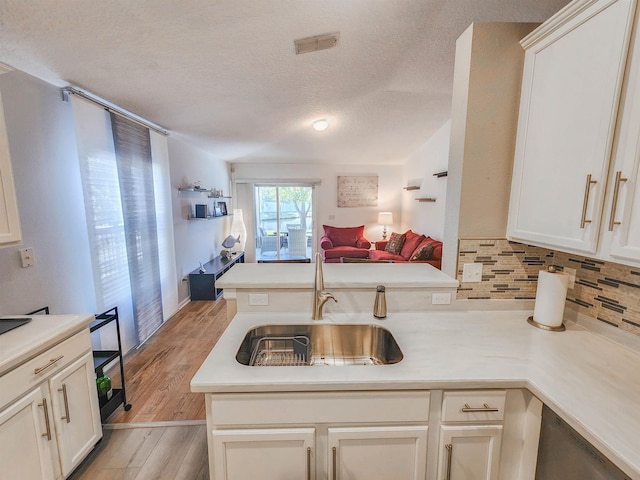 kitchen with sink, kitchen peninsula, a textured ceiling, decorative backsplash, and light wood-type flooring