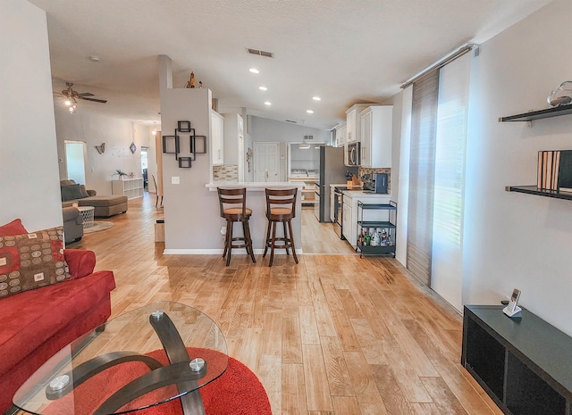 living room with light wood-type flooring, vaulted ceiling, and ceiling fan