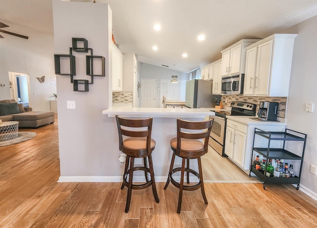 kitchen with white cabinets, vaulted ceiling, light wood-type flooring, appliances with stainless steel finishes, and kitchen peninsula