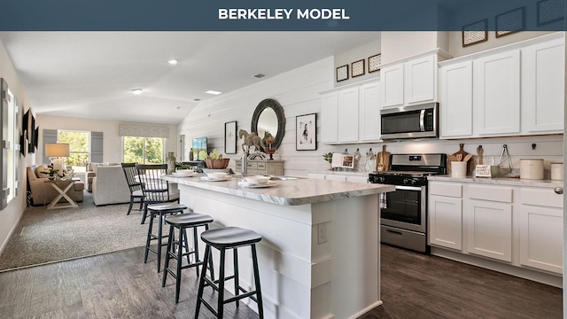 kitchen featuring dark wood finished floors, stainless steel appliances, vaulted ceiling, a kitchen bar, and open floor plan