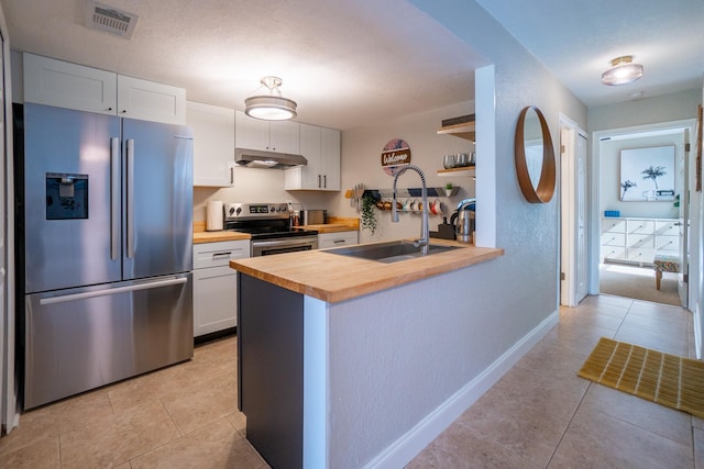 kitchen with stainless steel appliances, wood counters, under cabinet range hood, a sink, and light tile patterned floors