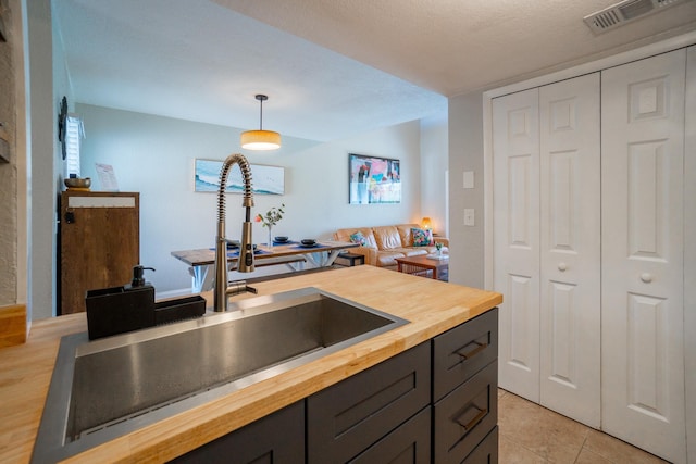 kitchen featuring wood counters, a sink, pendant lighting, and light tile patterned flooring