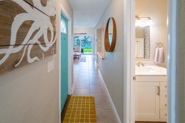 corridor with a textured wall, a sink, baseboards, and tile patterned flooring