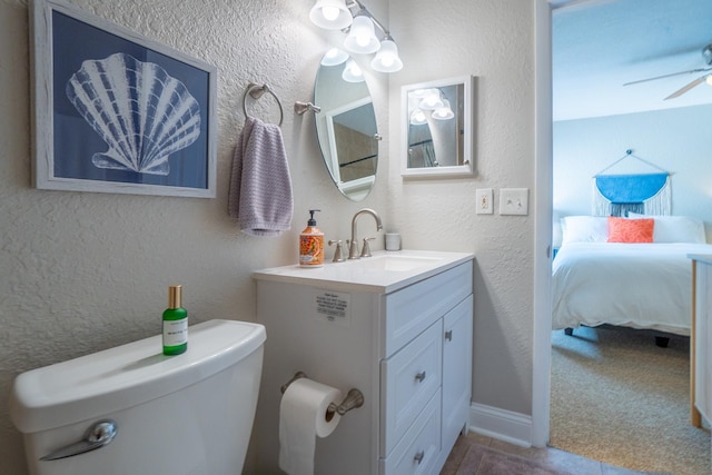 ensuite bathroom with toilet, a ceiling fan, a textured wall, and vanity