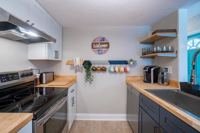 kitchen featuring stainless steel appliances, butcher block countertops, under cabinet range hood, baseboards, and white cabinets