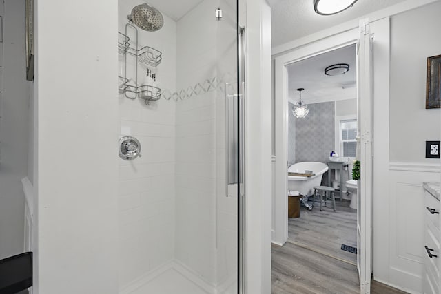 bathroom with wainscoting, a shower stall, a textured ceiling, wood finished floors, and a freestanding tub