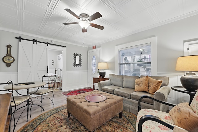 living area featuring a barn door, wainscoting, light wood-style flooring, and an ornate ceiling