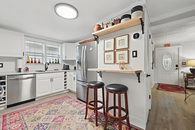 kitchen featuring a breakfast bar, a sink, white cabinets, light countertops, and appliances with stainless steel finishes