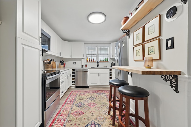 kitchen featuring stainless steel appliances, butcher block countertops, a sink, white cabinets, and a kitchen breakfast bar