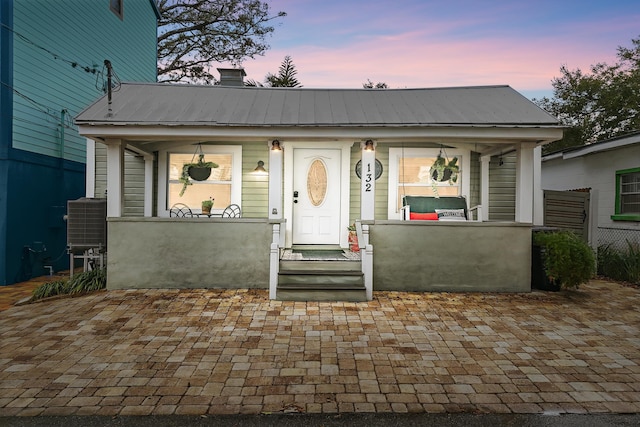 view of front of house featuring a chimney, a porch, a standing seam roof, metal roof, and fence