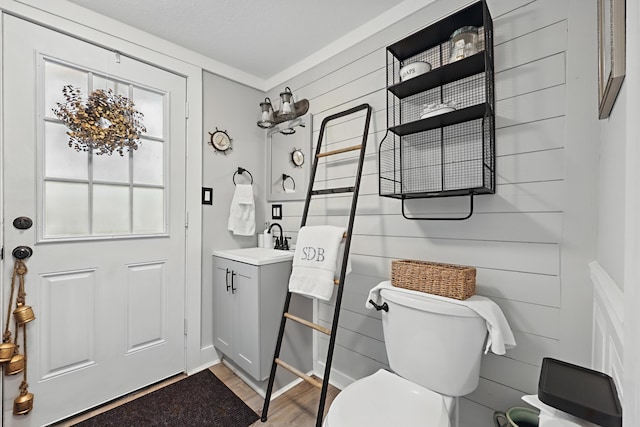 half bathroom with wooden walls, vanity, toilet, and wood finished floors