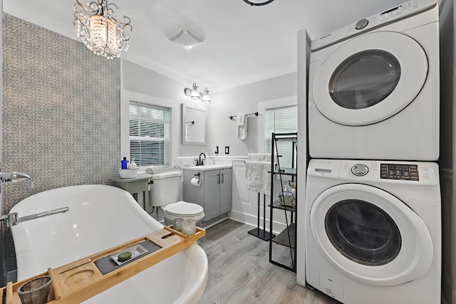 laundry area with light wood-type flooring, stacked washing maching and dryer, laundry area, and a notable chandelier