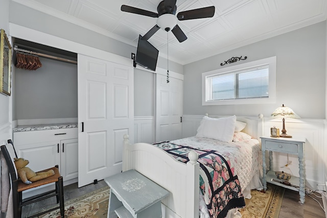 bedroom with a wainscoted wall, dark wood-type flooring, ornamental molding, and an ornate ceiling