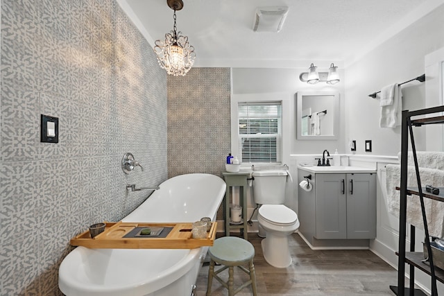 bathroom with a freestanding bath, toilet, wood finished floors, and vanity