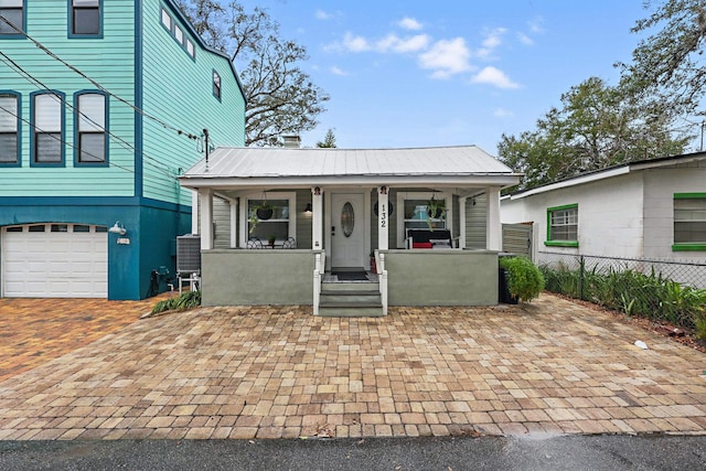 view of front of house with metal roof, covered porch, a garage, fence, and decorative driveway