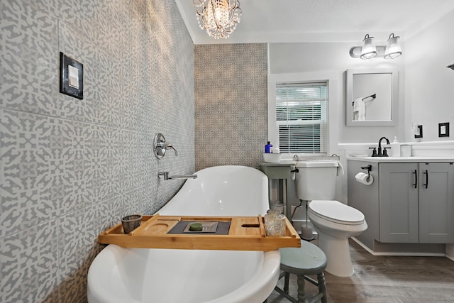 bathroom with toilet, wood finished floors, vanity, a freestanding tub, and tile walls