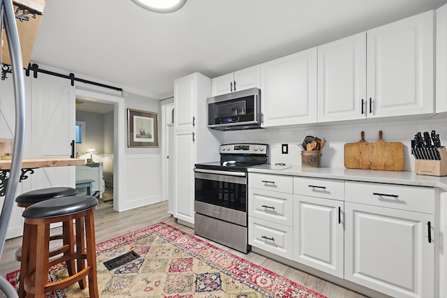 kitchen with light countertops, a barn door, appliances with stainless steel finishes, light wood-style floors, and white cabinetry