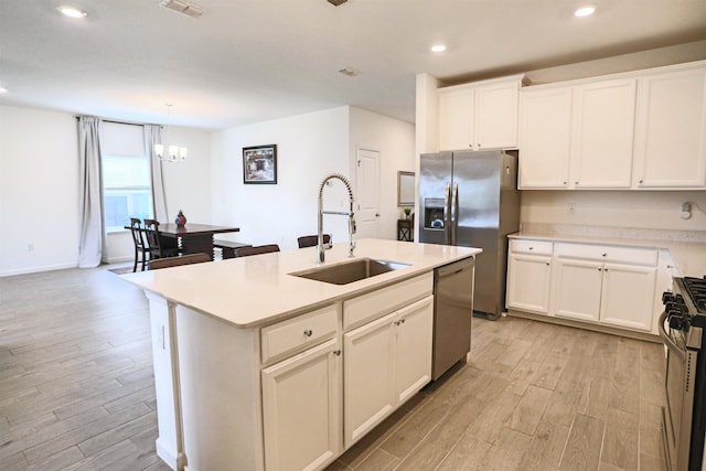 kitchen with a kitchen island with sink, sink, appliances with stainless steel finishes, and light hardwood / wood-style flooring