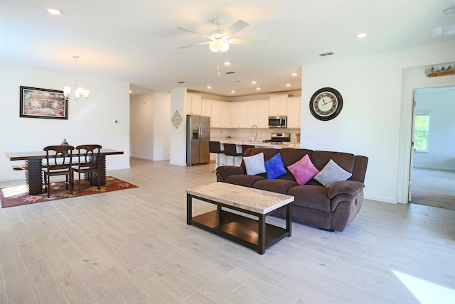 living room with ceiling fan with notable chandelier, light wood-type flooring, and sink