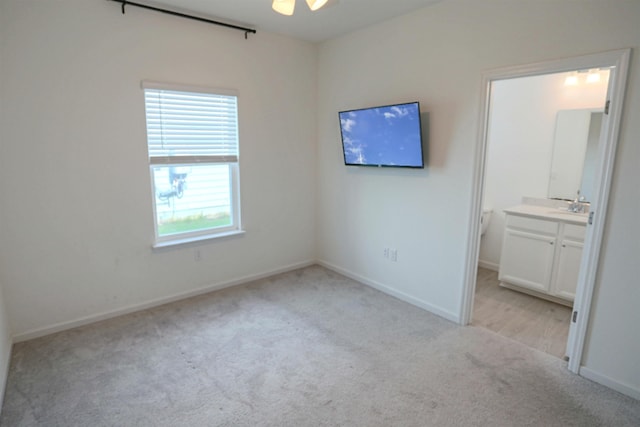 unfurnished bedroom featuring light carpet, ensuite bathroom, ceiling fan, and sink