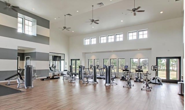 gym featuring light hardwood / wood-style flooring, a towering ceiling, and french doors