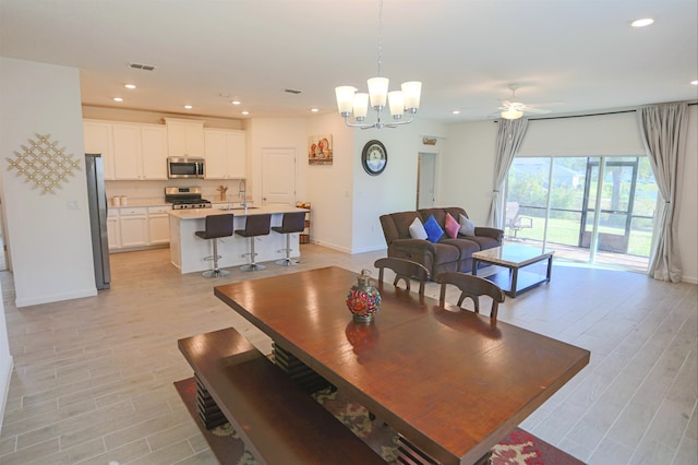 dining space featuring ceiling fan with notable chandelier, light hardwood / wood-style floors, and sink