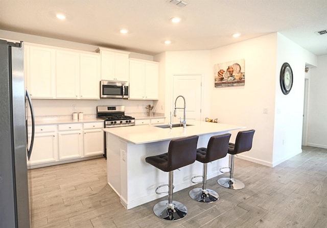 kitchen with white cabinetry, sink, stainless steel appliances, a kitchen island with sink, and a breakfast bar