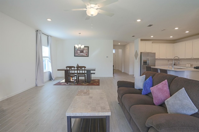 living room with sink, light hardwood / wood-style floors, and ceiling fan with notable chandelier