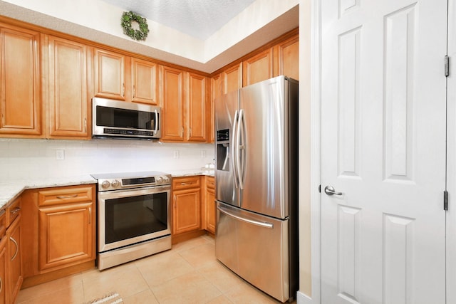 kitchen featuring light stone counters, a textured ceiling, decorative backsplash, light tile patterned floors, and appliances with stainless steel finishes