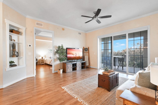 living room featuring built in shelves, light hardwood / wood-style floors, ceiling fan, and ornamental molding