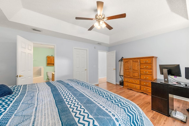 bedroom with ensuite bathroom, hardwood / wood-style floors, ceiling fan, a raised ceiling, and a textured ceiling